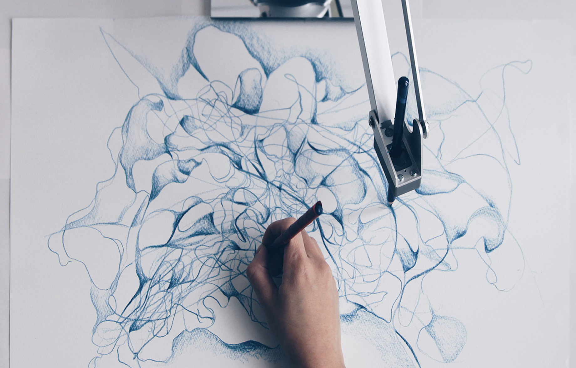 A hand and a robotic arm drawing together in blue on a large sheet of paper