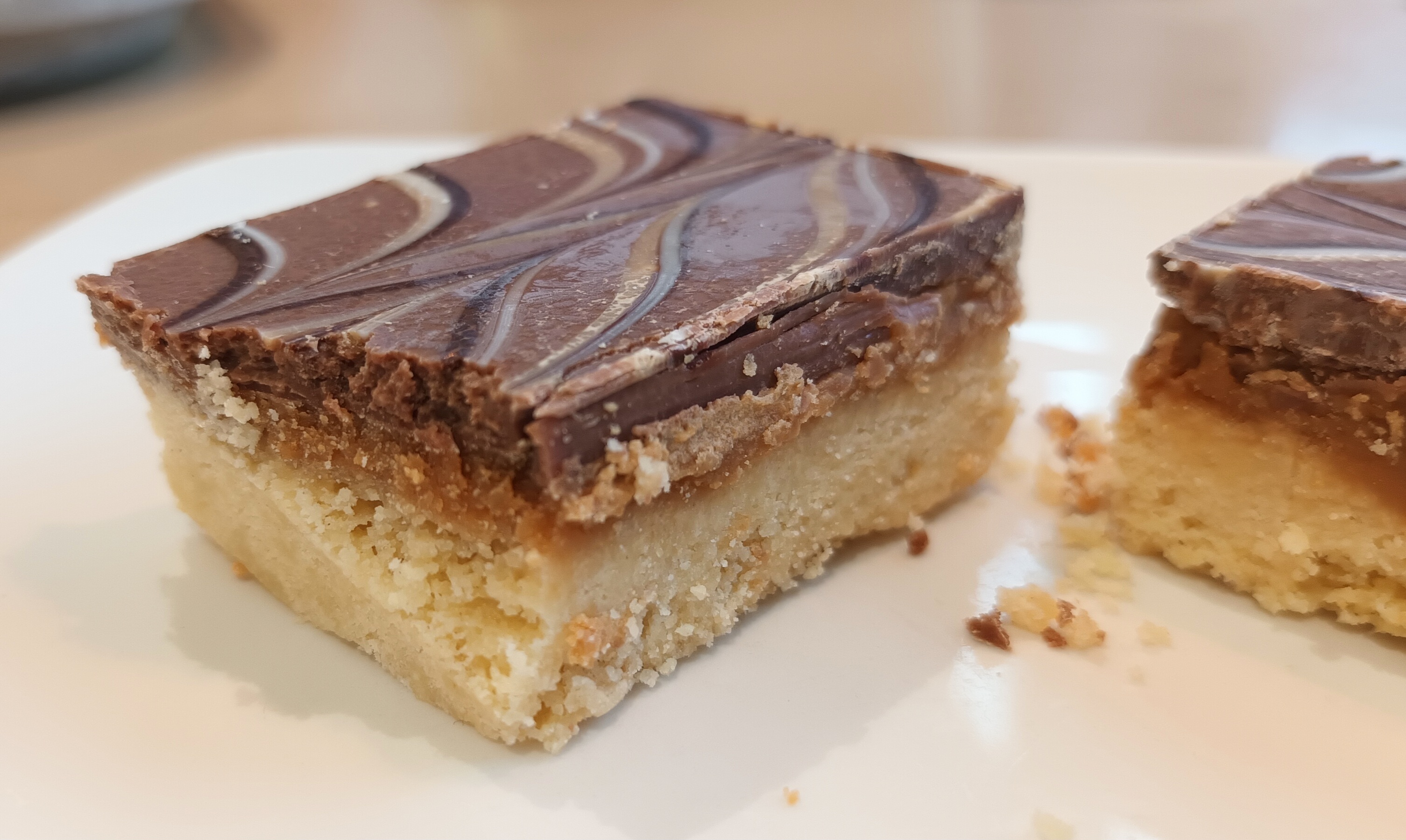 Photo of a slice of millionair's shortbread cut in two, showing layers of shortbread biscuit, caramel and chocolate.
