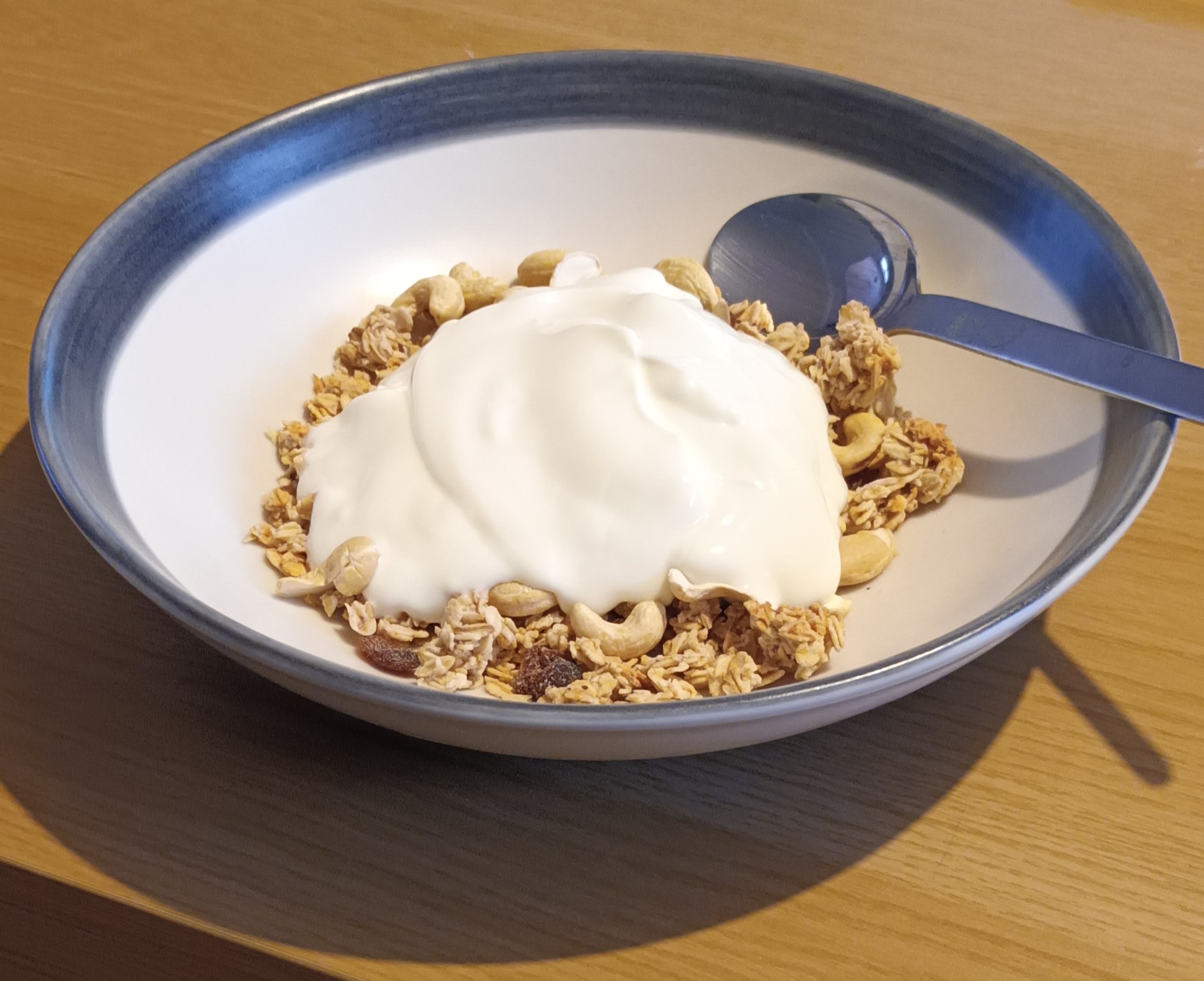 Photo of a dollop of yoghurt on top of some breakfast cereal in a bowl with a spoon.
